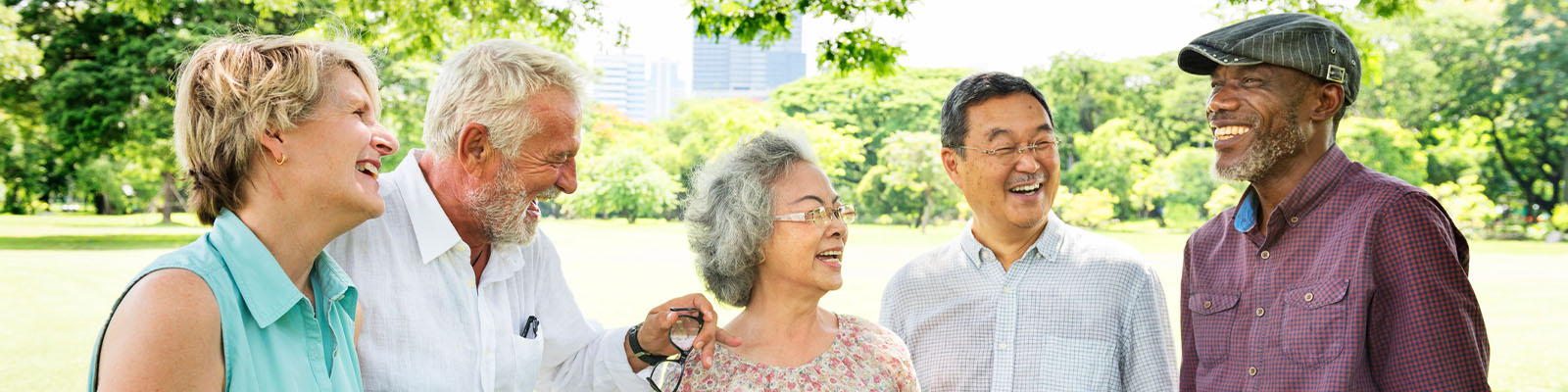 A group of senior men and women standing outdoors smiling and laughing while looking at each other