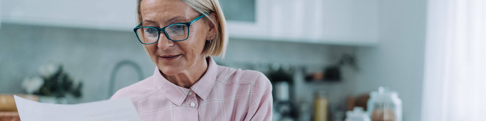 A senior woman wearing reading glasses looking down at a document she is holding