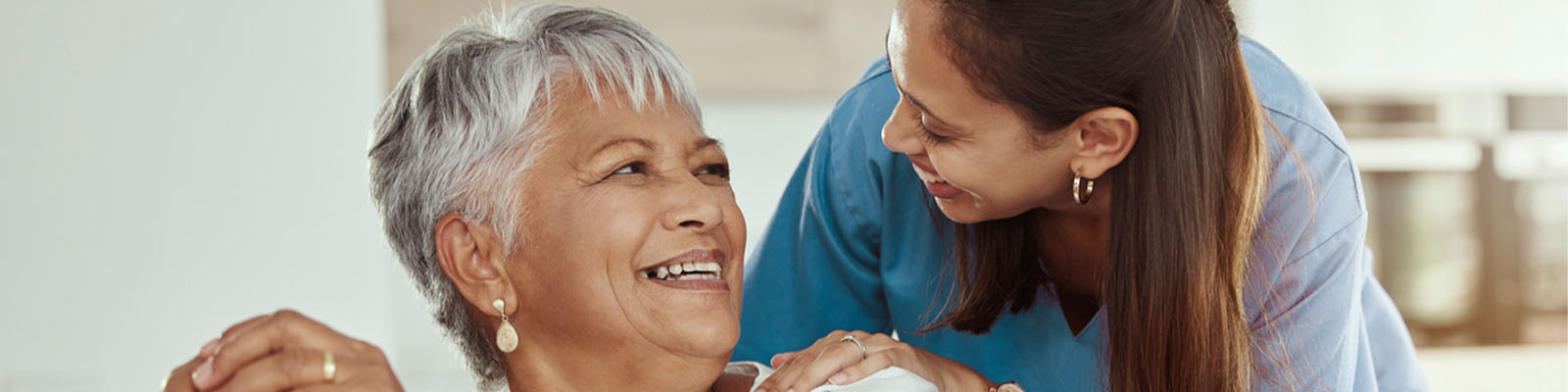 A senior woman holding onto her wooden cane while looking up at her female nursing assistant while smiling