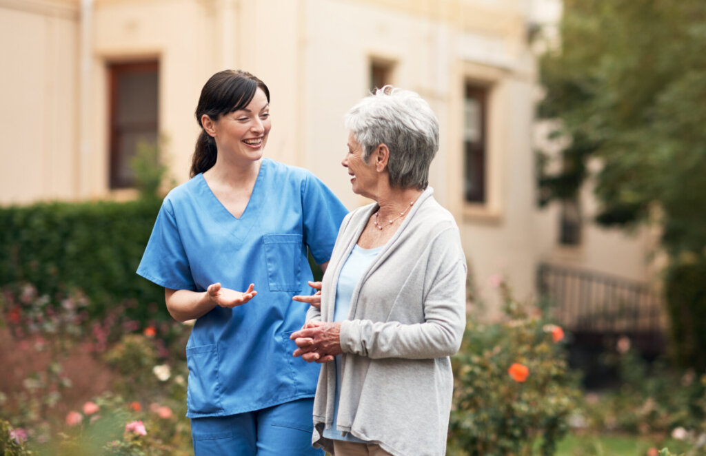 A senior woman walking outdoors with a nursing assistant at a senior living community